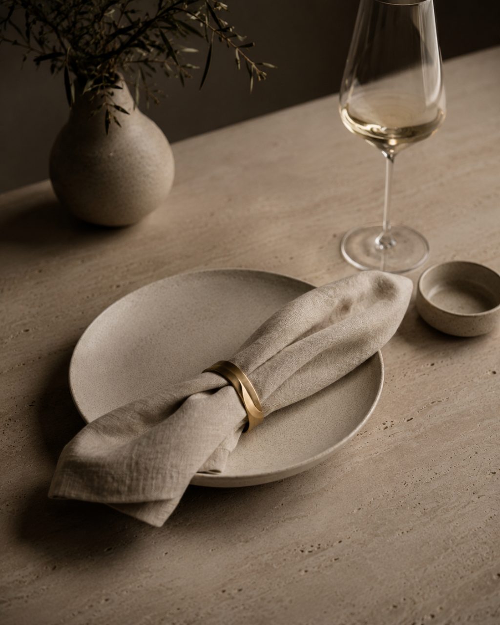 Quiet Celebration — a pared-back place setting of stoneware, linen and a single brass bowl on a stone table.